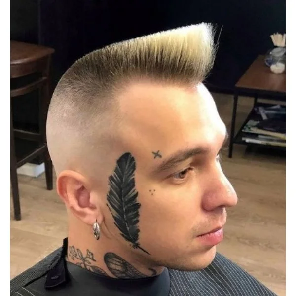 um homem com Blonde Psycho Quiff e várias tatuagens no dito que inclui uma pena
